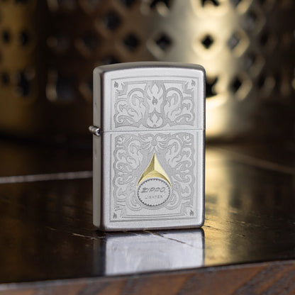 Lifestyle image of Zippo Vintage Filigree Design Satin Chrome Windproof Lighter standing on a dark wooden table showing the front of the lighter with a decorative metal candle holder as the background. 

